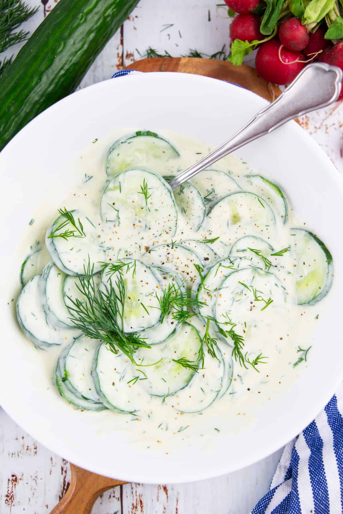 creamy vegan cucumber salad in a white bowl with a spoon 