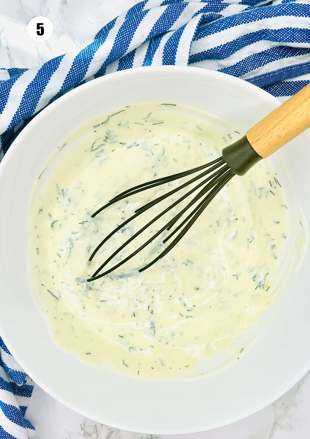 dill yogurt dressing in a white bowl with a black whisk 