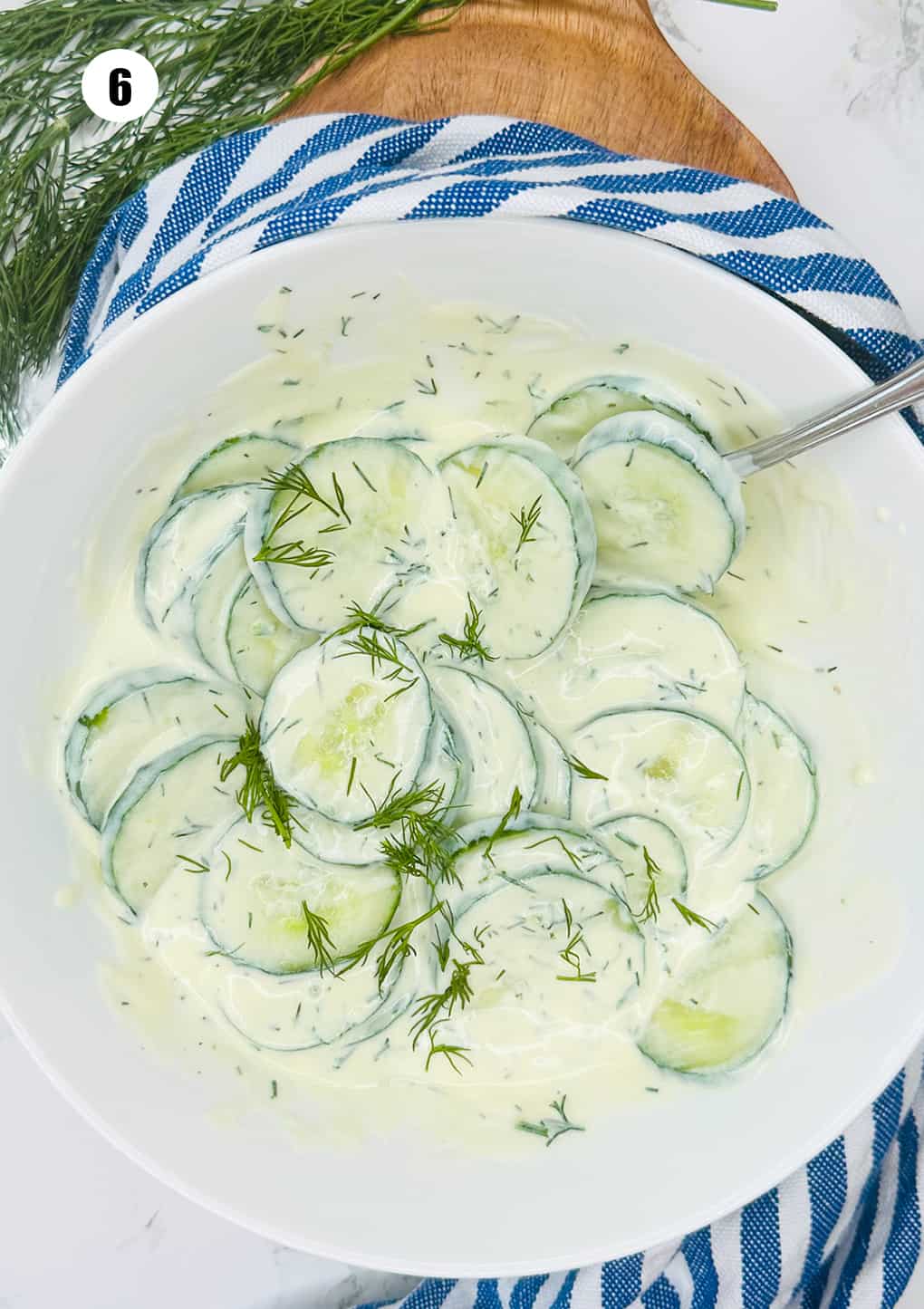 dill cucumber salad with vegan yogurt dressing in a white bowl on a wooden board 