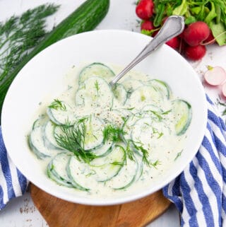 a white bowl with dill cucumber salad with radishes and a cucumber in the background
