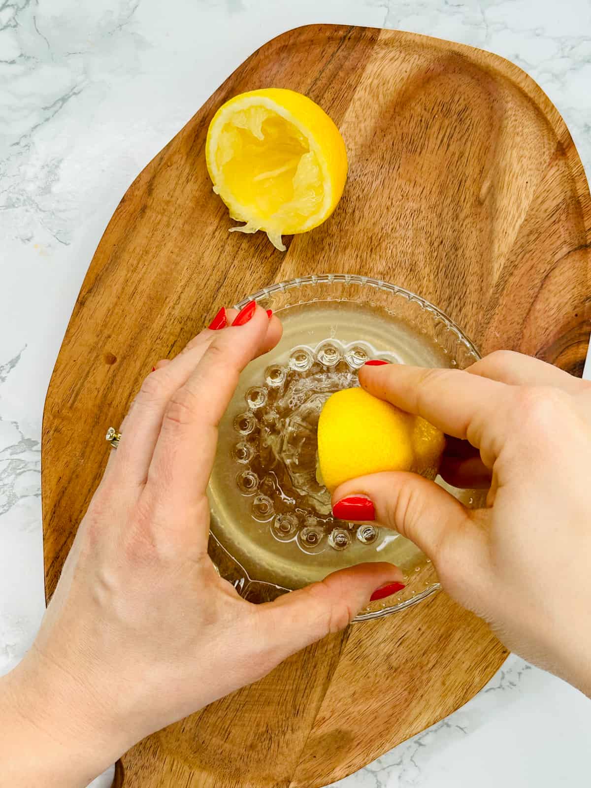 a hand juicing a lemon with a glass juicer on a wooden chopping board 