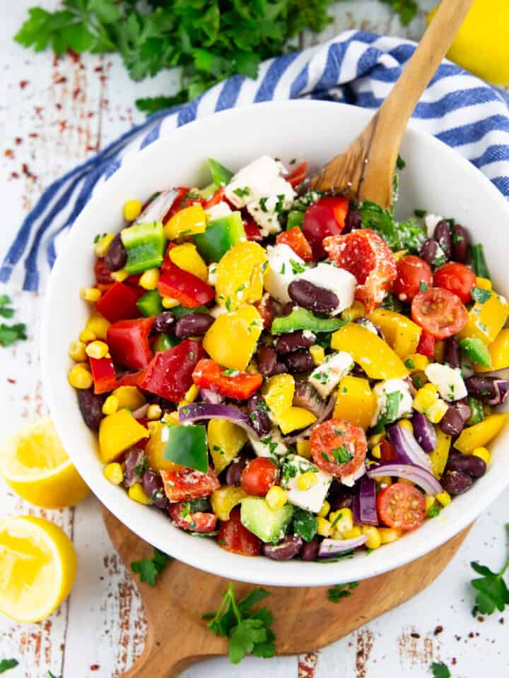 a kidney bean salad in a white bowl with a wooden spoon on a marble countertop