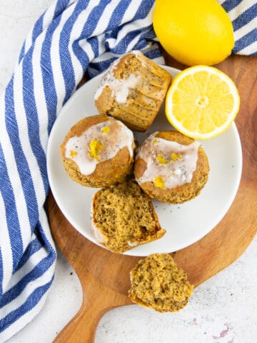 four lemon poppy seed muffins on a white plate on a wooden board