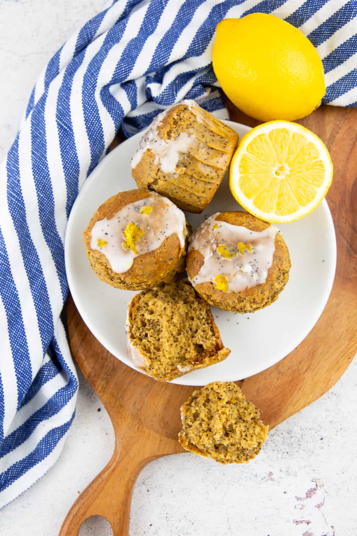 four lemon poppy seed muffins on a white plate on a wooden board 