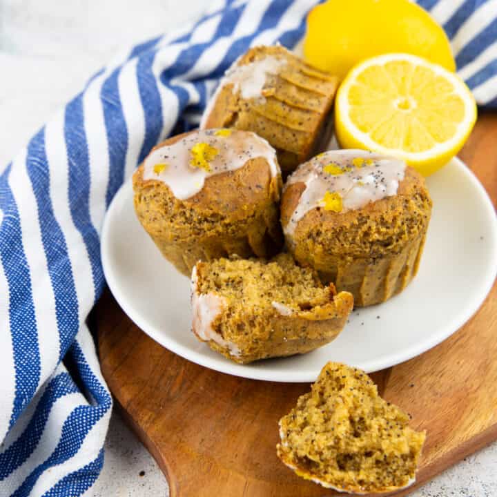 four lemon poppy seed muffins on a white plate on a wooden board
