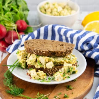 a vegan egg salad sandwich on a white plate with radishes in the background