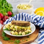a vegan egg salad sandwich on a white plate with radishes in the background