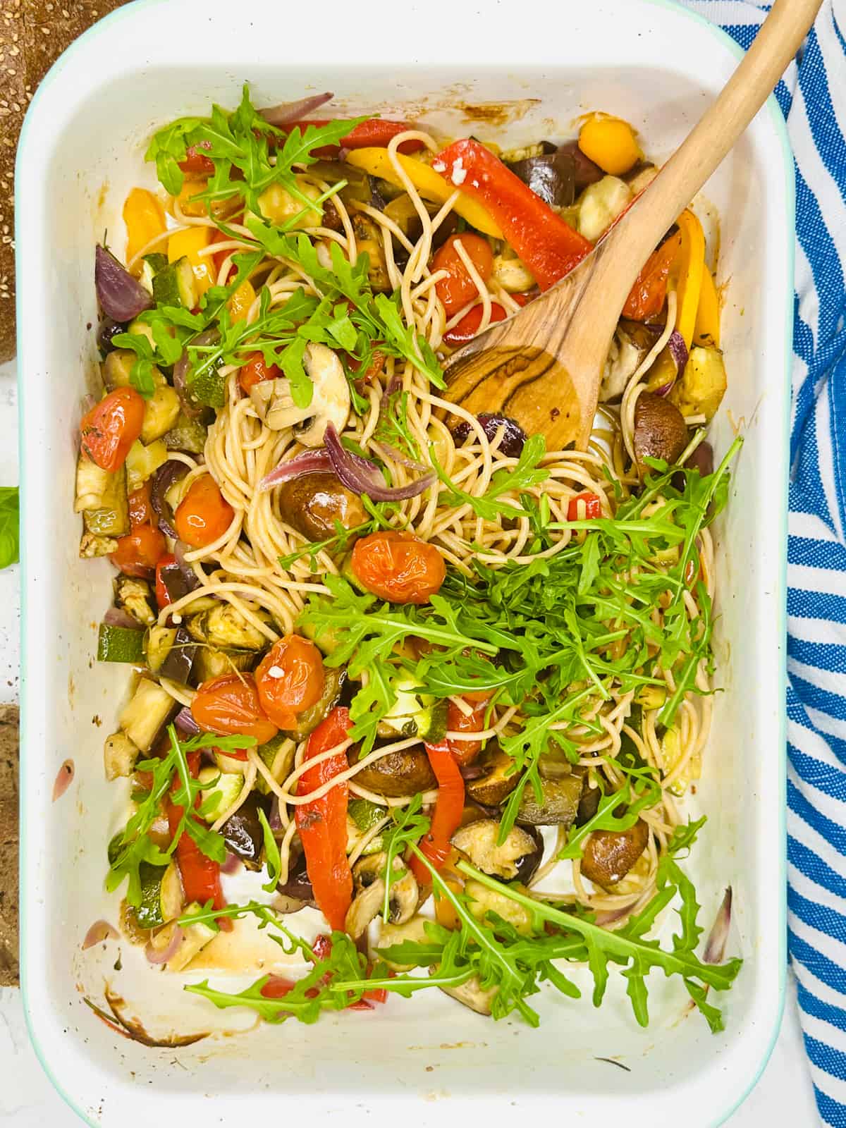 roasted vegetables with spaghetti in a white baking dish with a wooden spoon 