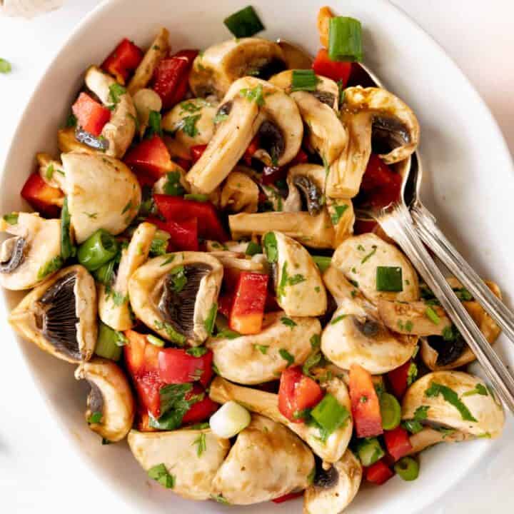 a mushroom salad with bell pepper and parsley in a white bowl with cutlery