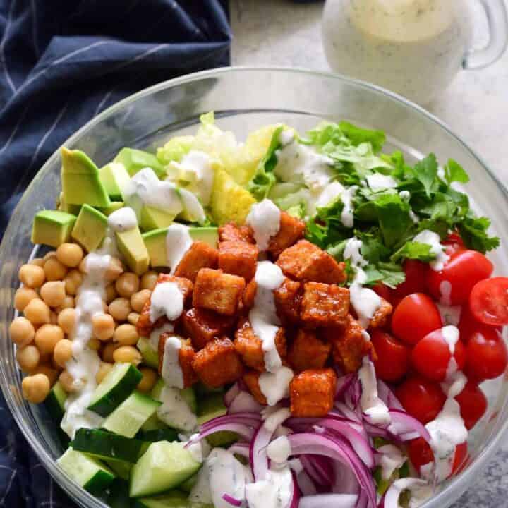 a glass bowl with lettuce, tomatoes, cucumber, and BBQ tofu