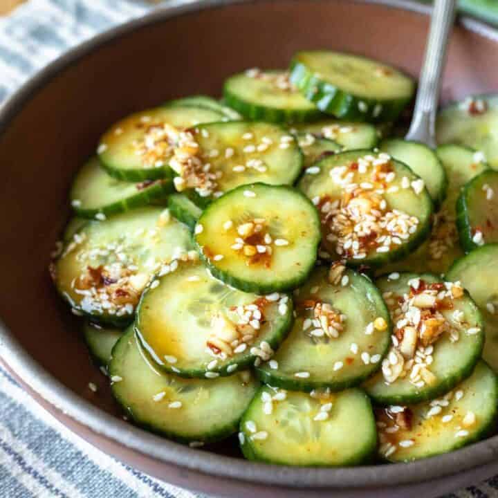 cucumber salad with Asian dressing in a brown bowl on a striped table cloth