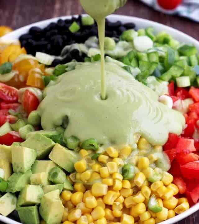 avocado dressing being poured over a bowl with corn, avocado, and black beans