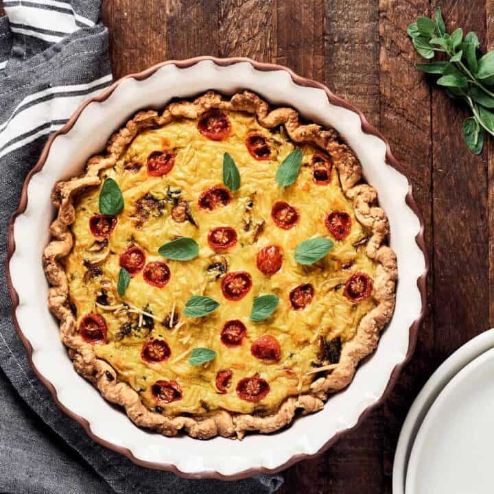 a vegan quiche with tomatoes in a white quiche dish on a wooden board