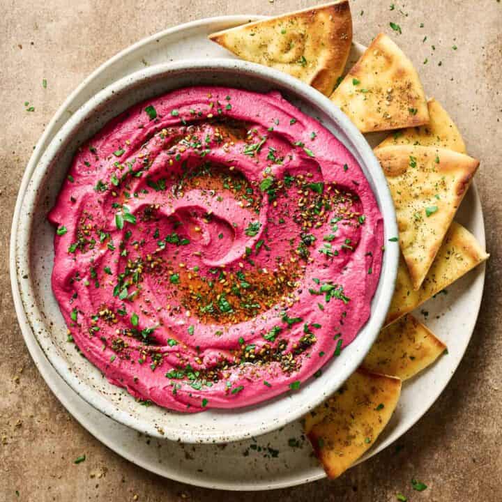 a small grey bowl with beet hummus with pita triangles on the side