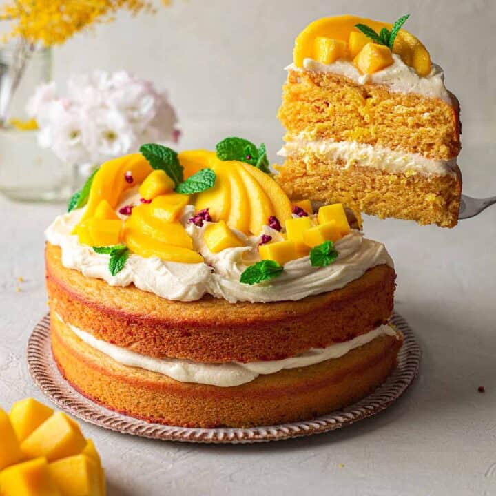 a vegan mango cake with one slice on a cake lifter