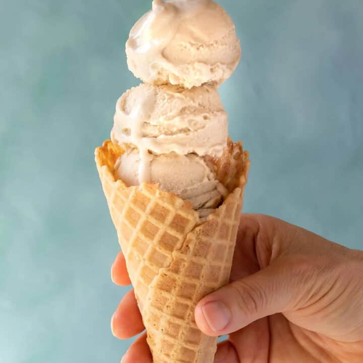 a hand holding an ice cream cone with three scoops of vanilla oat ice cream