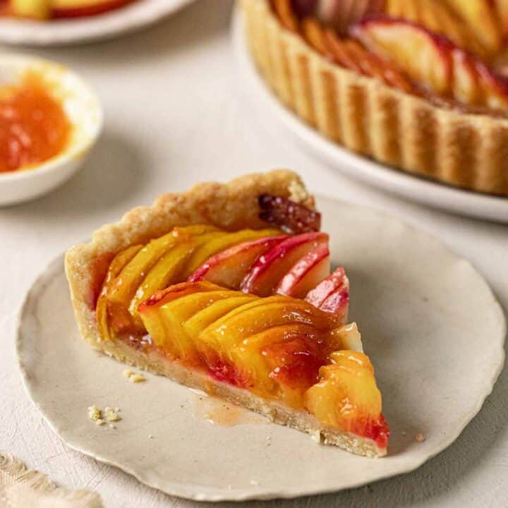a slice of vegan peach tart on a beige plate with more cake in the background