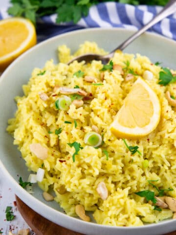 a grey bowl with lemon rice on a wooden board with parsley in the background