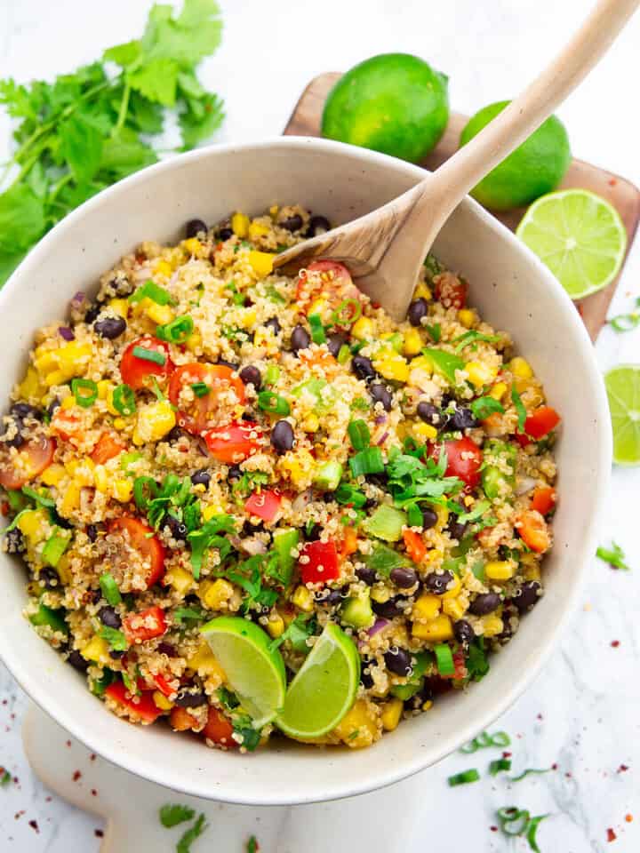 a white bowl with quinoa black bean salad on a marble countertop with limes in the background