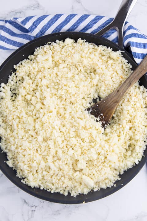 cauliflower rice in a black pan with a wooden spoon