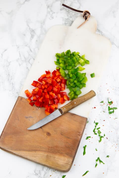 chopped green and red bell pepper on a chopping board with a knife
