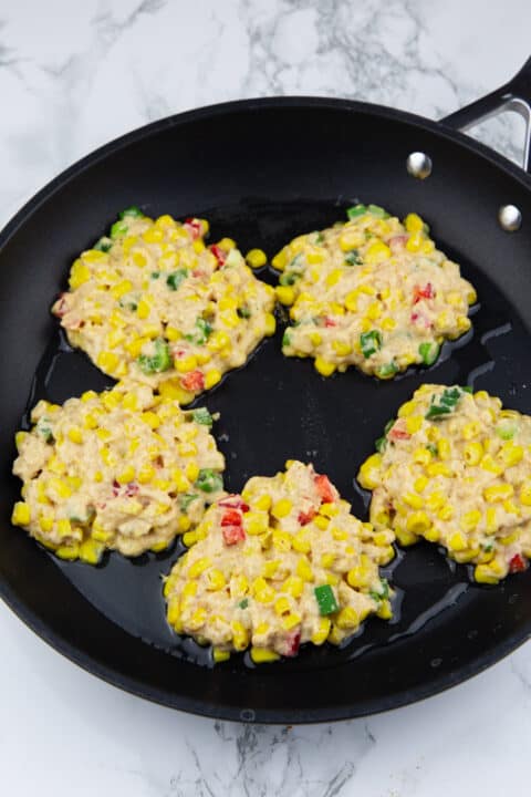 five corn fritters in a black pan before frying