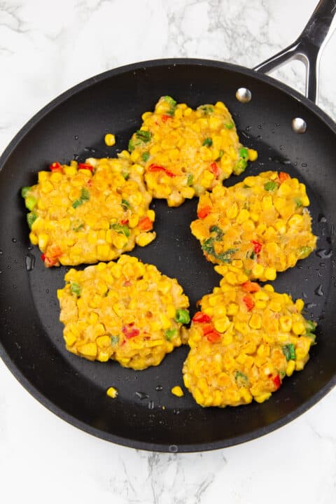 five corn fritters in a black pan after frying