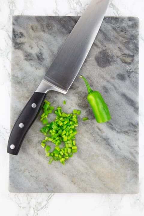 chopped jalapeños on a chopping board with a large knife on the side