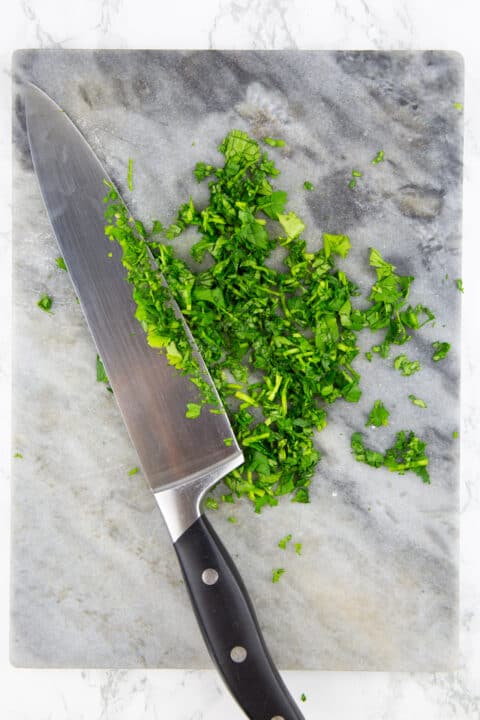 chopped cilantro on a chopping board with a large knife on the side