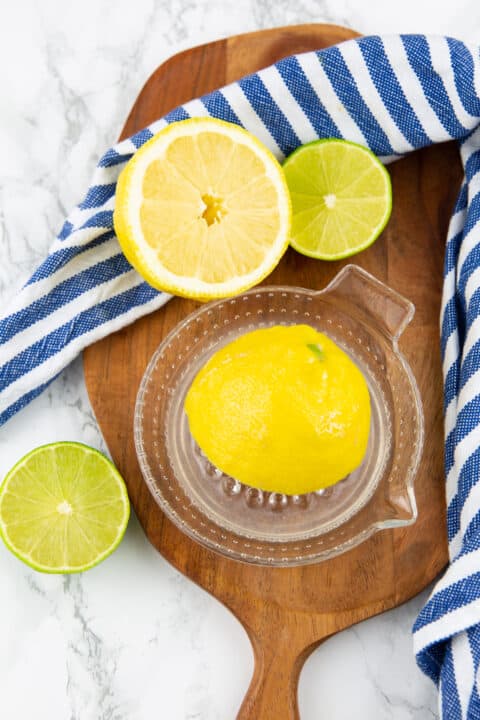 halved lemon and lime with a glass juicer on a wooden board