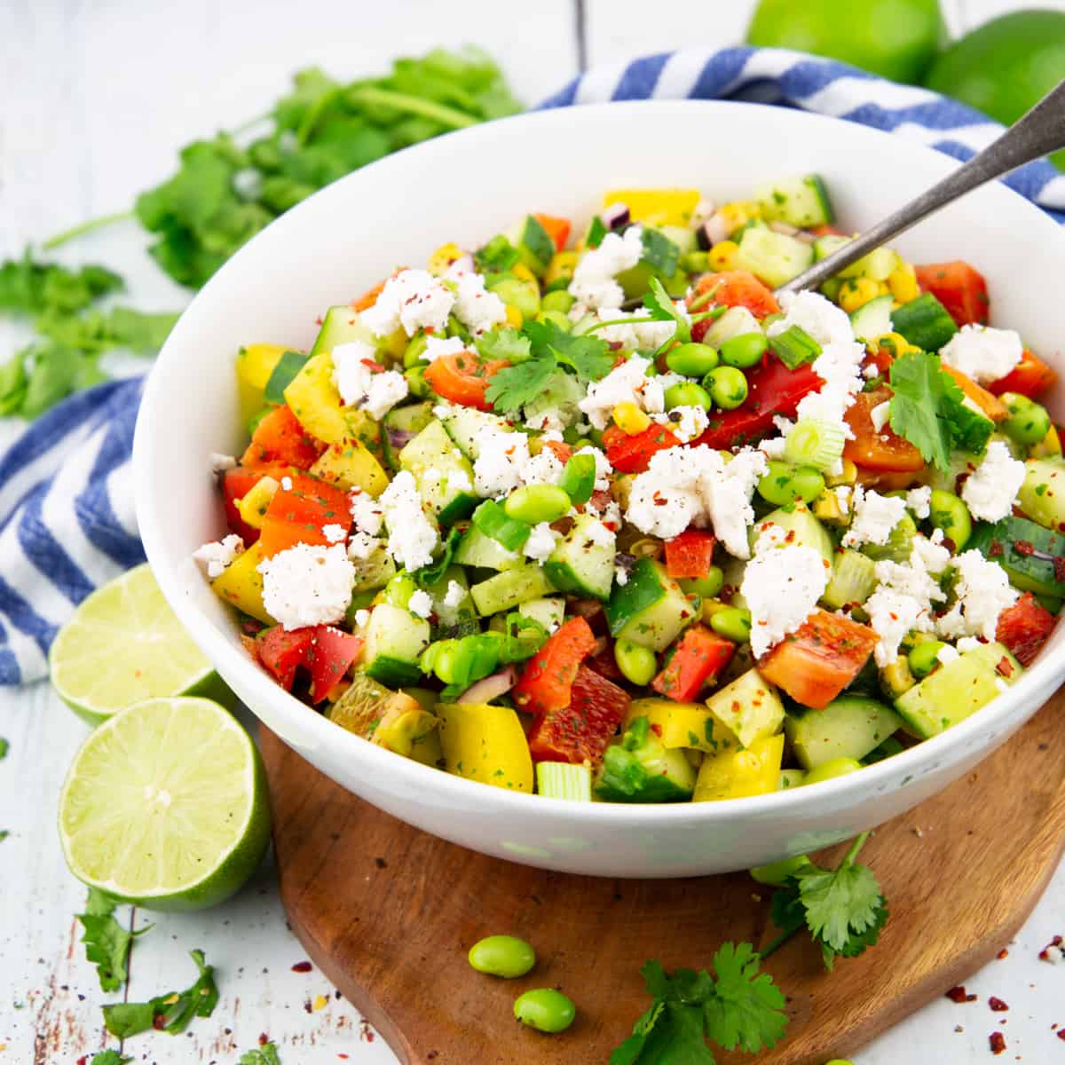 a white bowl with edamame salad on a wooden board with limes and fresh cilantro in the background