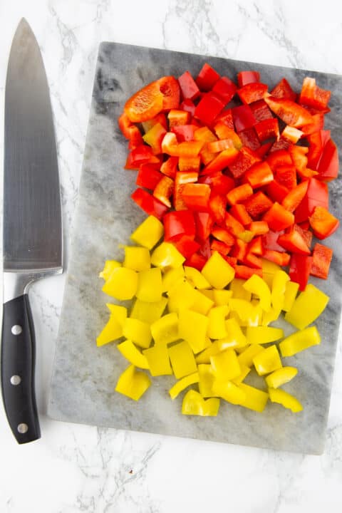 diced red and yellow bell pepper on a chopping board with a knife on the side