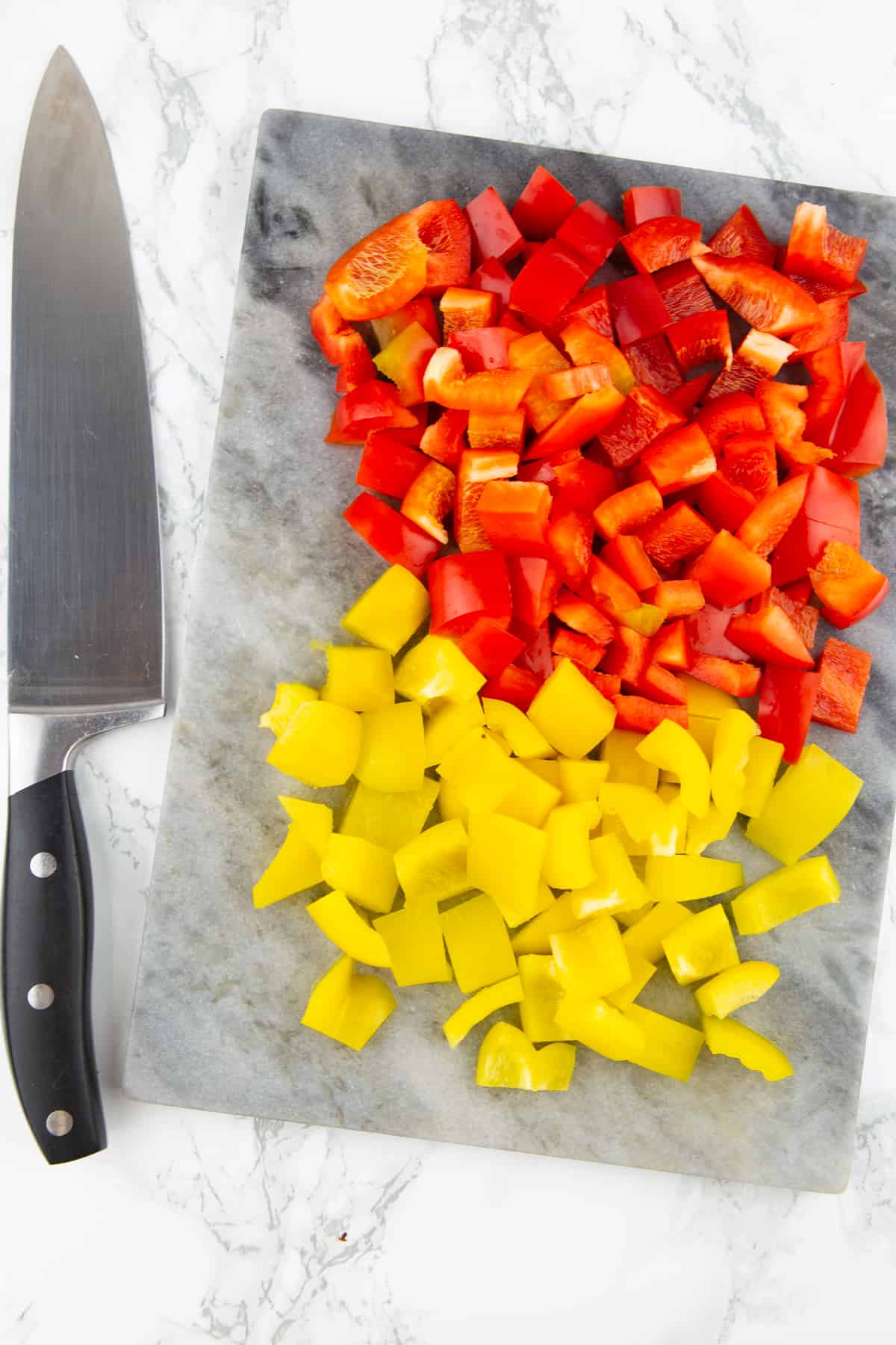 diced red and yellow bell pepper on a chopping board with a knife on the side