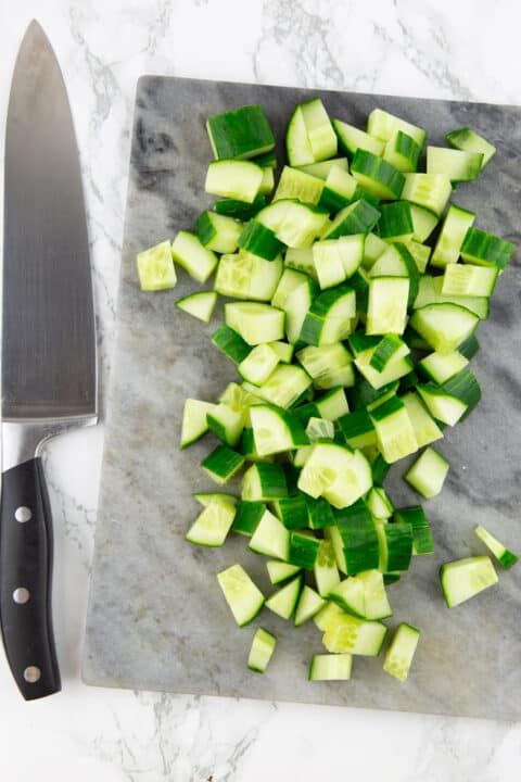 diced cucumber on a chopping board with a knife on the side