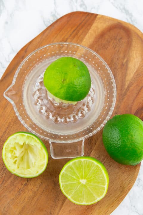 four lime halves with a glass juicer on a wooden board