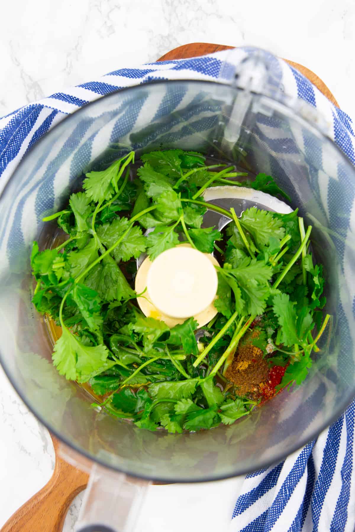 fresh cilantro and spices in a food processor on a wooden board