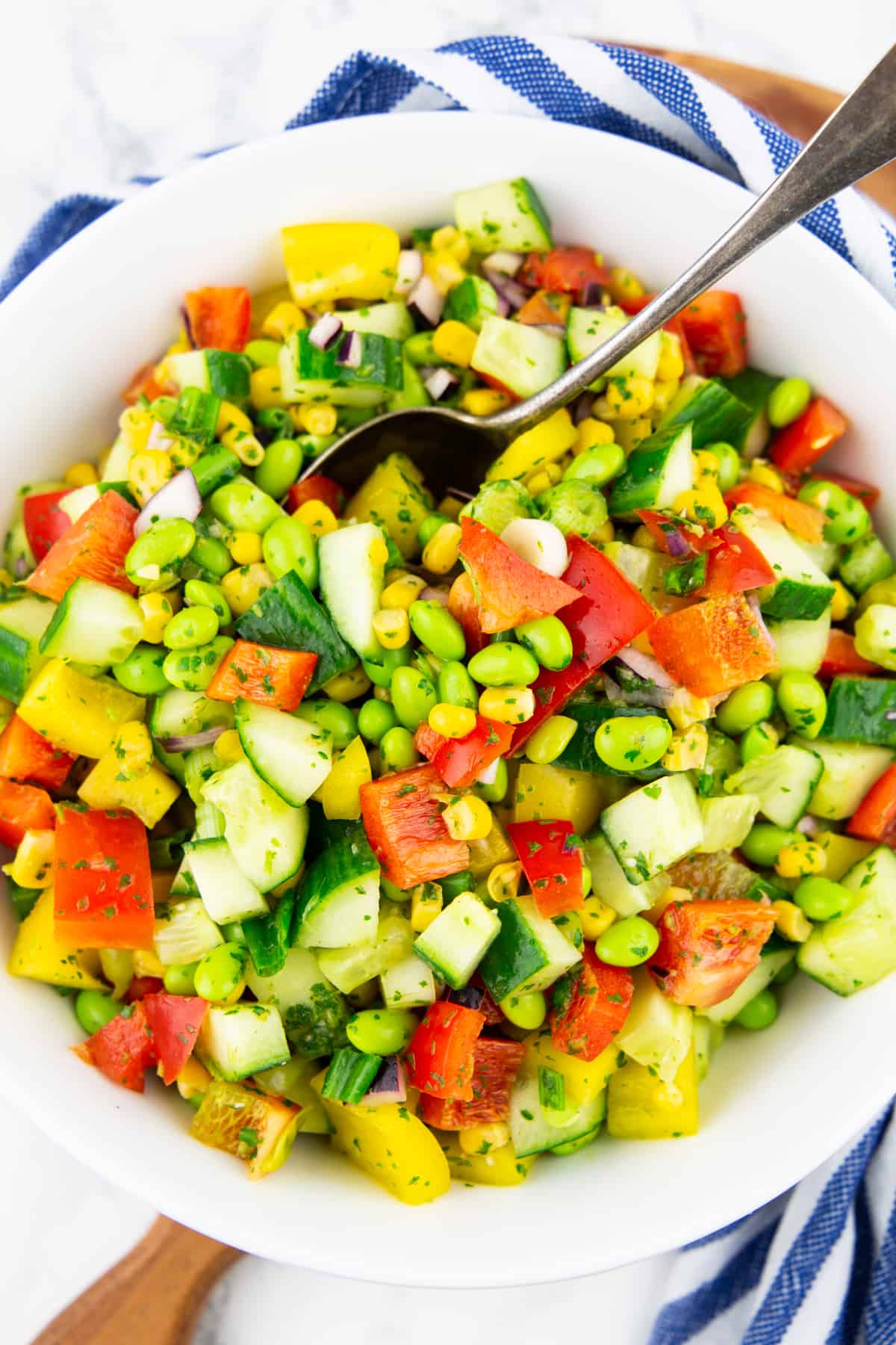 a white bowl with edamame salad with a spoon on a wooden board