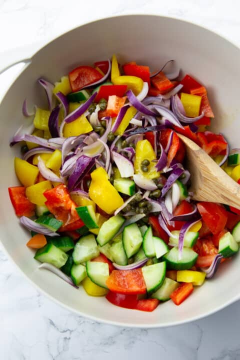 bell pepper, tomatoes, and cucumber with dressing in a grey bowl with a wooden spoon