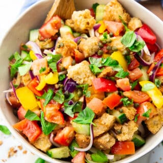 Panzanella in a white bowl with a wooden spoon on a marble countertop