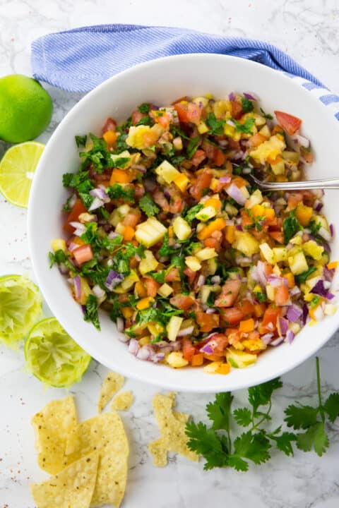 pineapple salsa in a white bowl with a spoon on a marble countertop