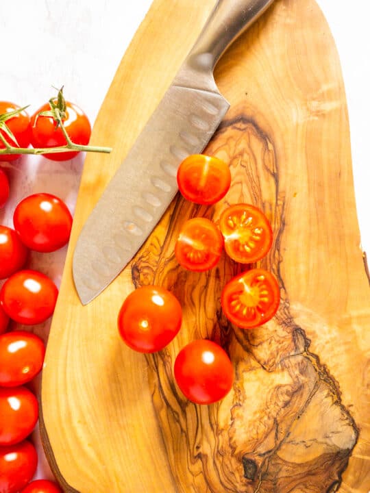 halved cherry tomatoes on a wooden chopping board with a knife