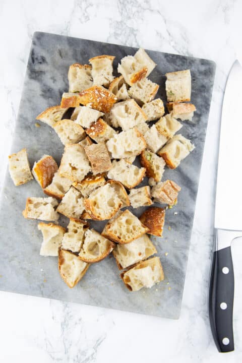 ciabatta bread cut into cubes on a marble chopping board with a large knife on the side