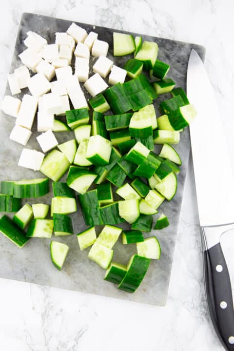 cubed vegan feta and cucumber on a chopping board with a knife on the side
