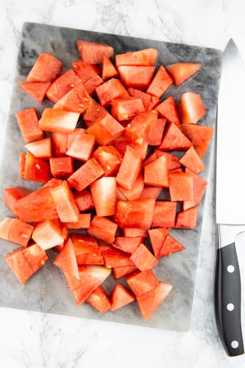 cubed watermelon on a chopping board with a knife on the side
