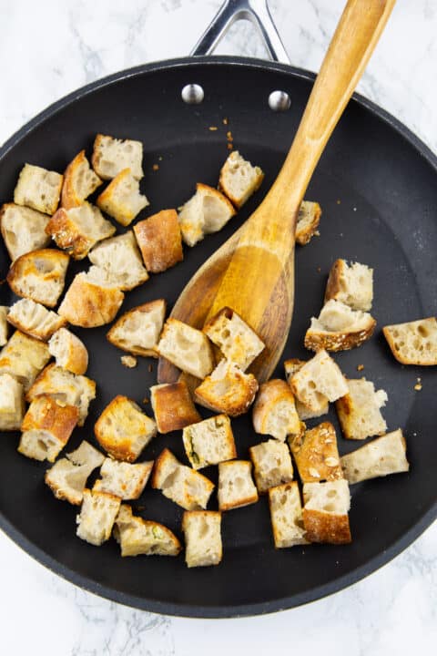crispy ciabatta bread croutons in a a black frying pan with a wooden spoon