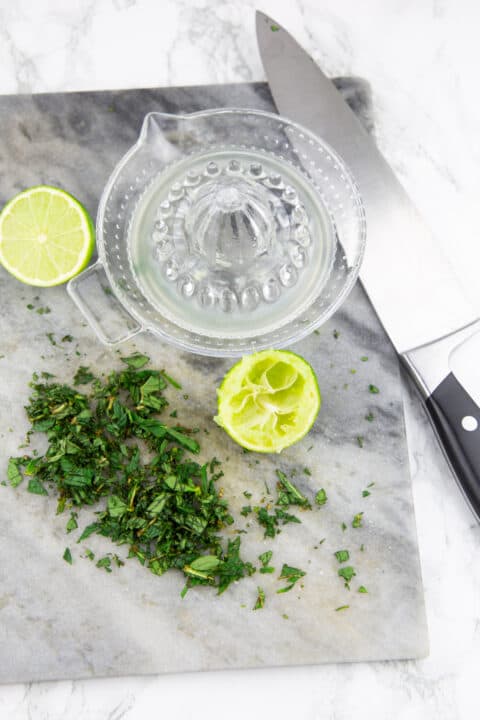 chopped mint and a glass juicer with two lime halves on a marble chopping board