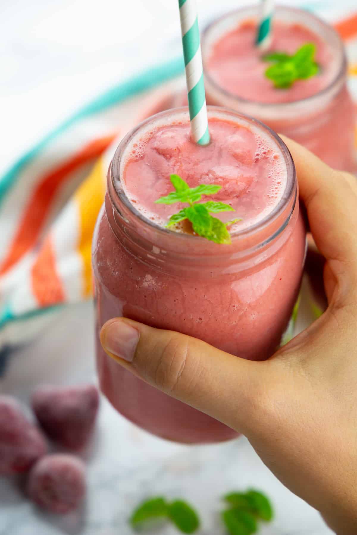 a hand holding a glass with watermelon smoothie with a white and blue straw 