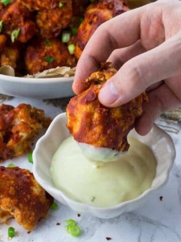 a hand dipping a cauliflower wing into a small bowl with vegan aioli