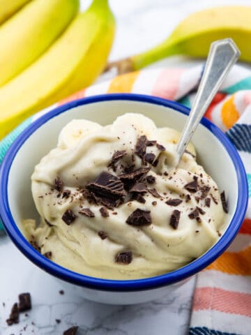 a blue and white bowl with frozen banana ice cream sprinkled with chopped dark chocolate