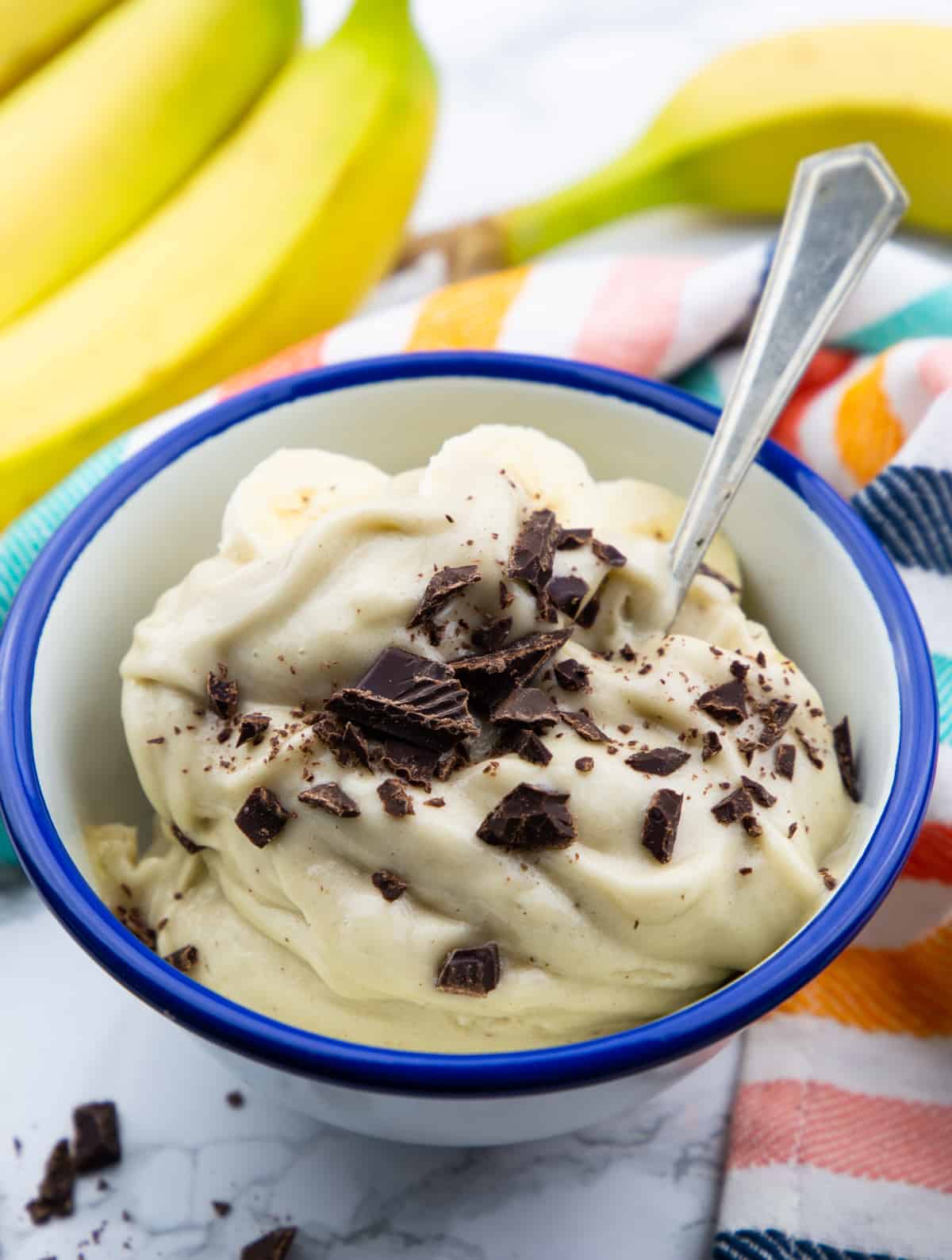 a blue and white bowl with frozen banana ice cream sprinkled with chopped dark chocolate 